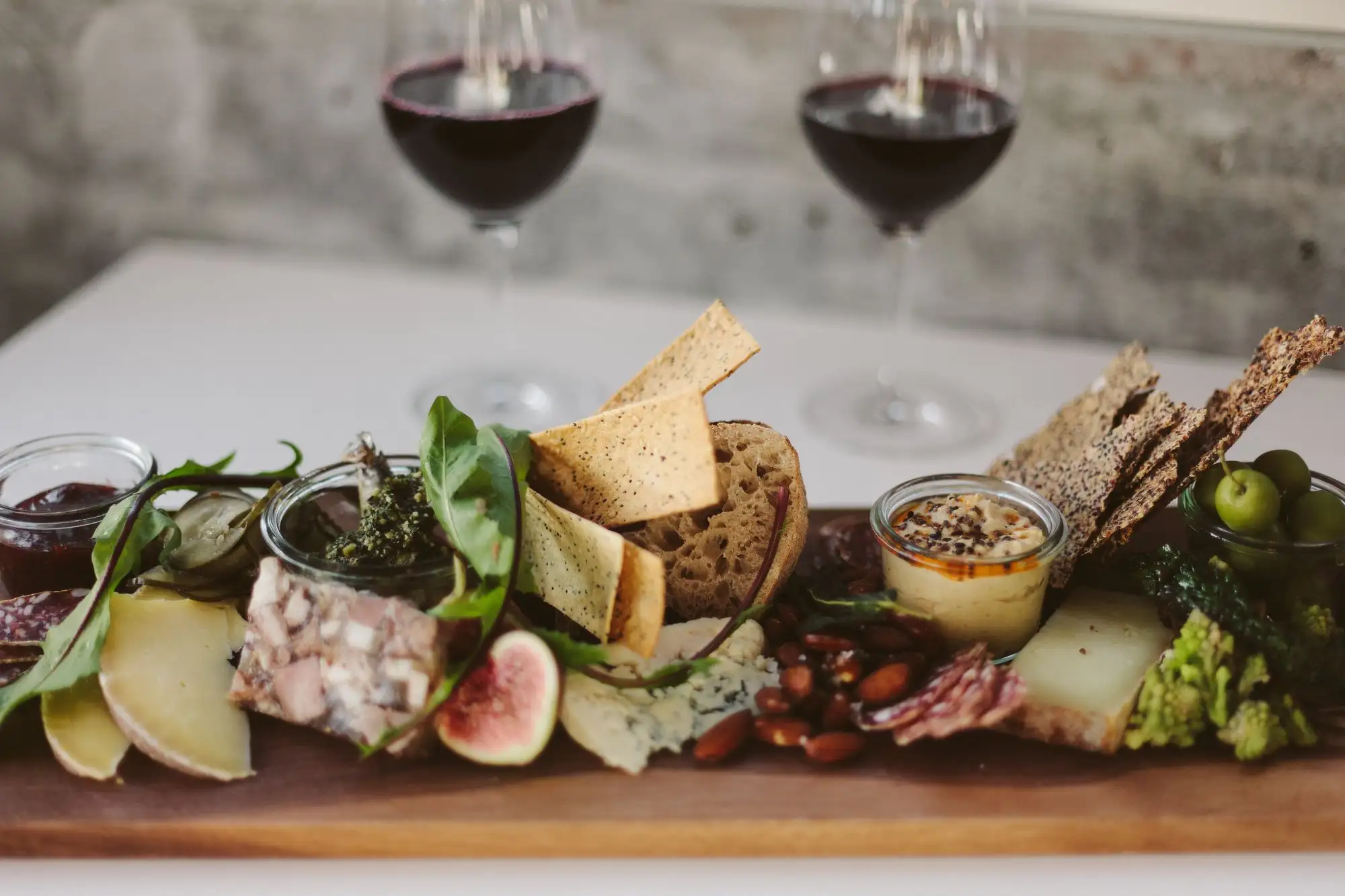 A cheese and charcuterie board with crackers, figs and dips in front of two glasses of red wine