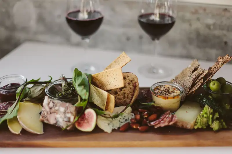 A cheese and charcuterie board with crackers, figs and dips in front of two glasses of red wine