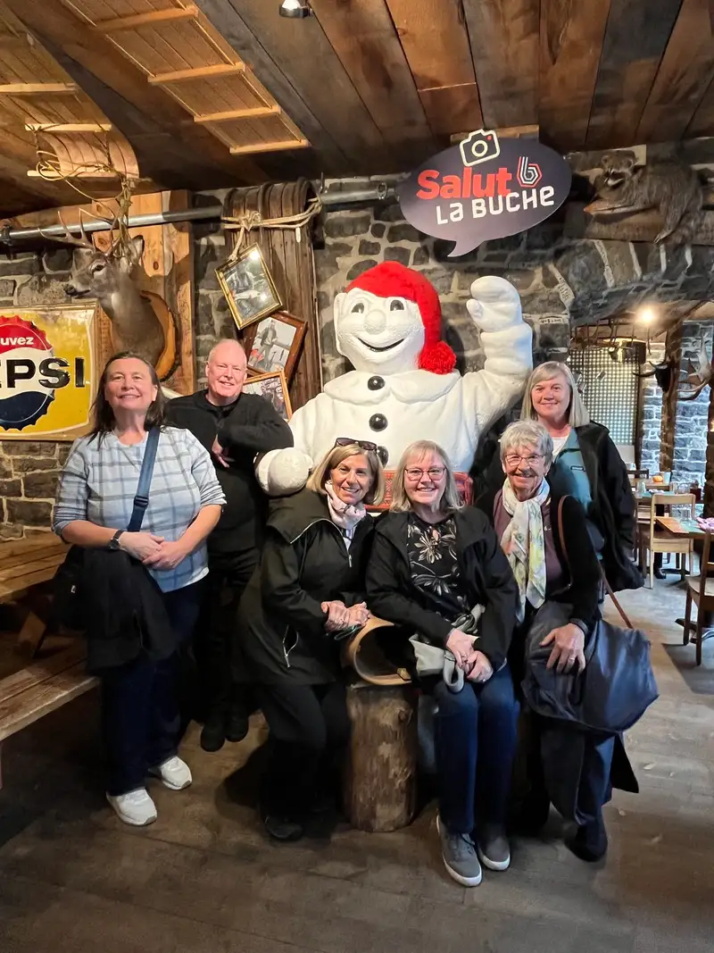 The group posing with a Bonhomme Carnaval figure inside a stone-walled Quebec City restaurant