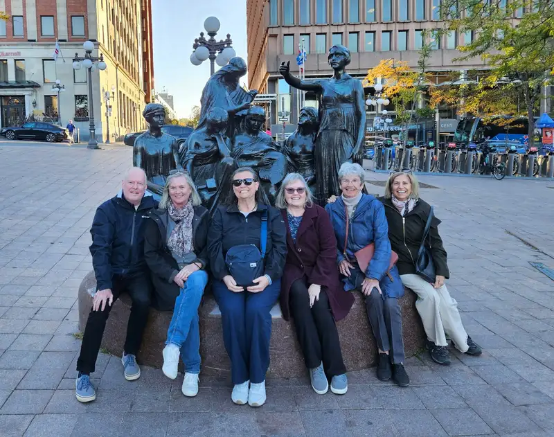 Six members sitting on the base of a bronze monument in a Quebec City square