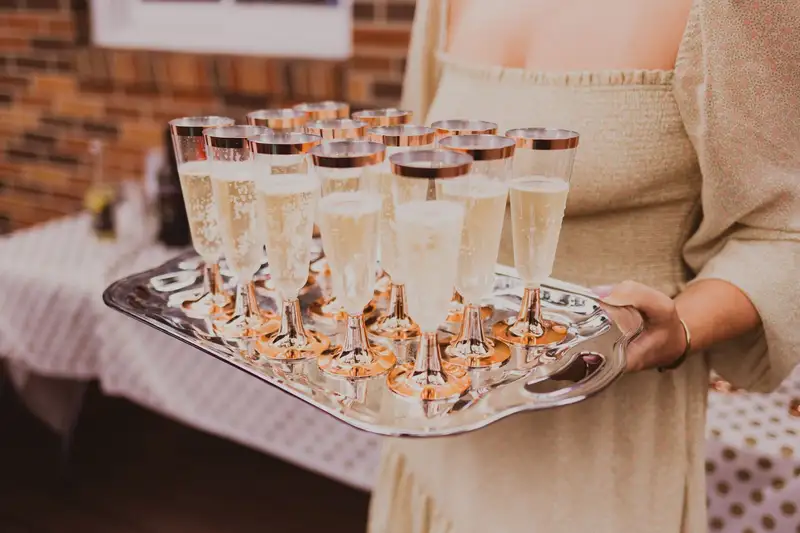 A server carrying a tray of sparkling wine flutes at an outdoor gathering