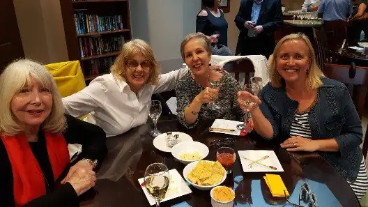 Four members smiling around a table with glasses of wine and plates of food at the 2017 summer party