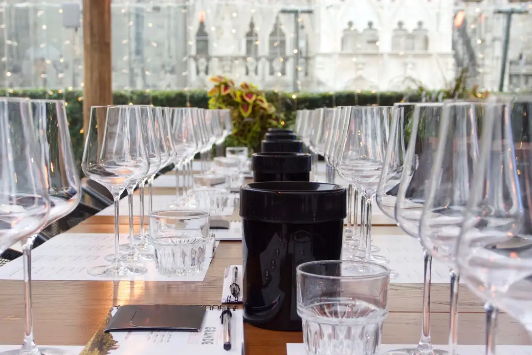 A long wooden table set with rows of wine glasses and tasting sheets under string lights