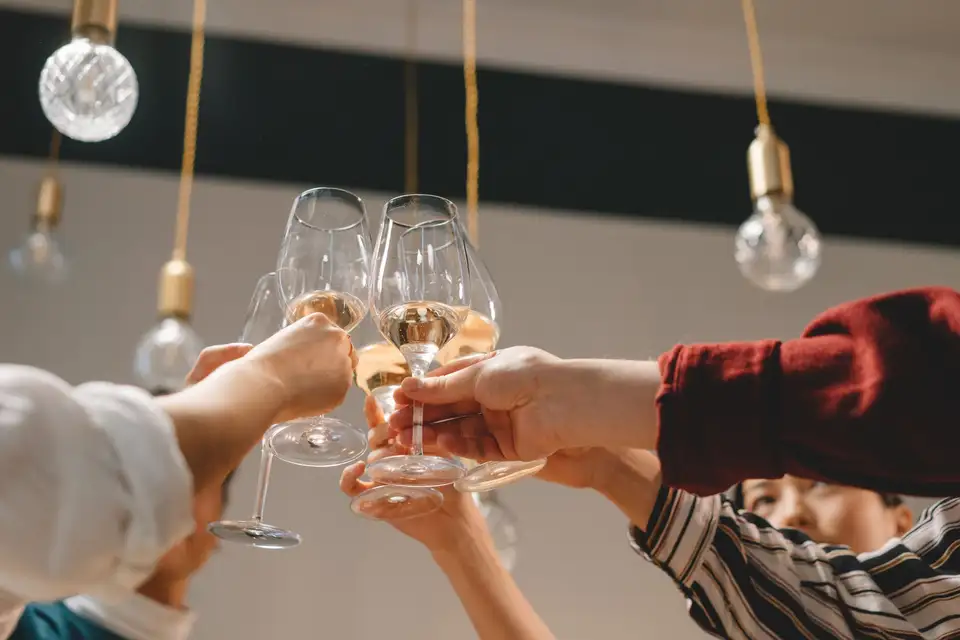 Hands raising glasses of white wine together under hanging lights